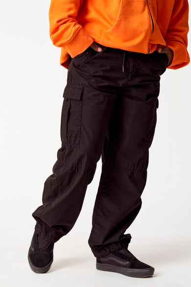 Pantalon cargo noir de COELY, avec des poches et une corde, combiné à un hoodie orange et des baskets noires.