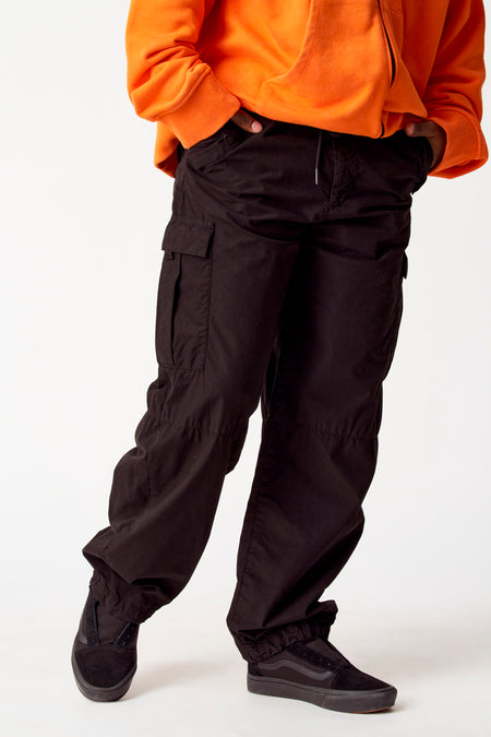 Pantalon cargo noir de COELY, avec des poches et une corde, combiné à un hoodie orange et des baskets noires.
