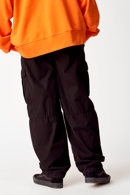 Pantalon cargo noir de COELY, avec une coupe décontractée et des poches sur les jambes, associé à un hoodie orange et des baskets noires.