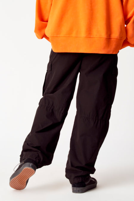 Pantalon cargo noir de COELY, porté avec un pull orange et des baskets noires à semelles brunes.