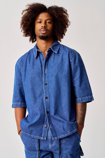 Chemise en jeans bleue de COELY, avec des manches courtes et des boutons noirs.