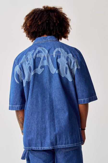 Chemise de jeans bleue de COELY, avec un grand motif de lettres sur le dos.