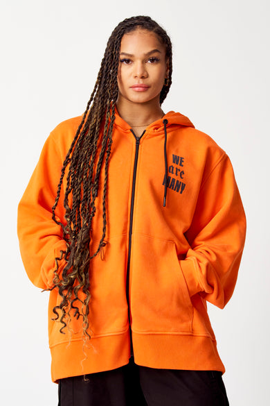 Gilet orange avec capuche COELY, avec fermeture éclair noire et impression texte "WE are MANY" sur la poitrine.