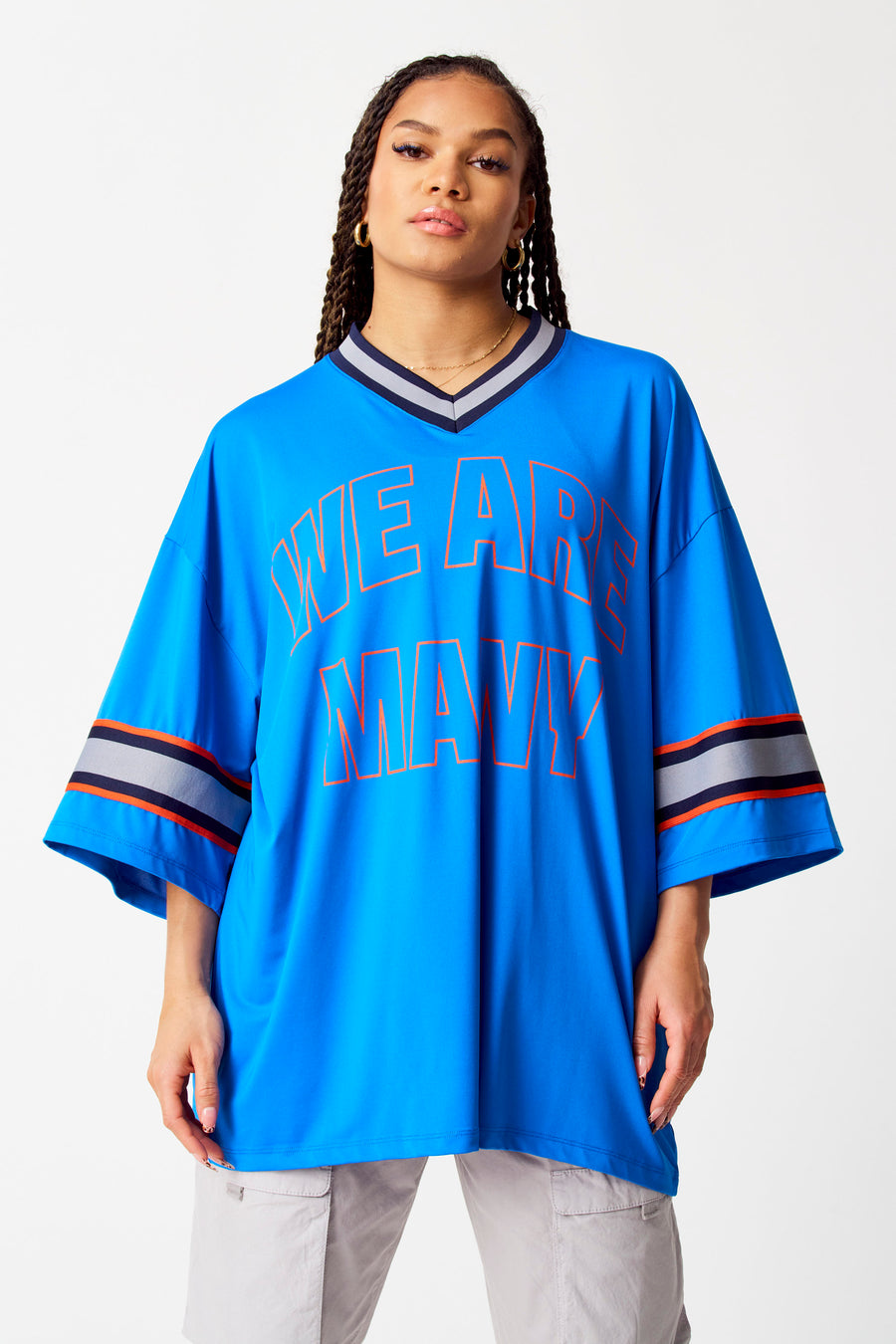 T-shirt bleu de COELY, avec un imprimé orange et des rayures sur les manches, porté avec un pantalon gris.