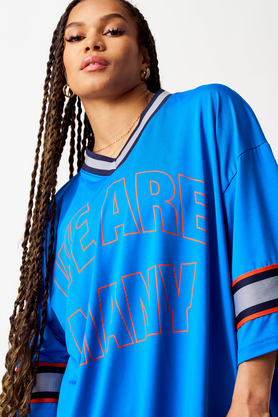 T-shirt bleu de COELY, avec des lettres oranges et des bordures rayées, porté avec des bijoux d'or.