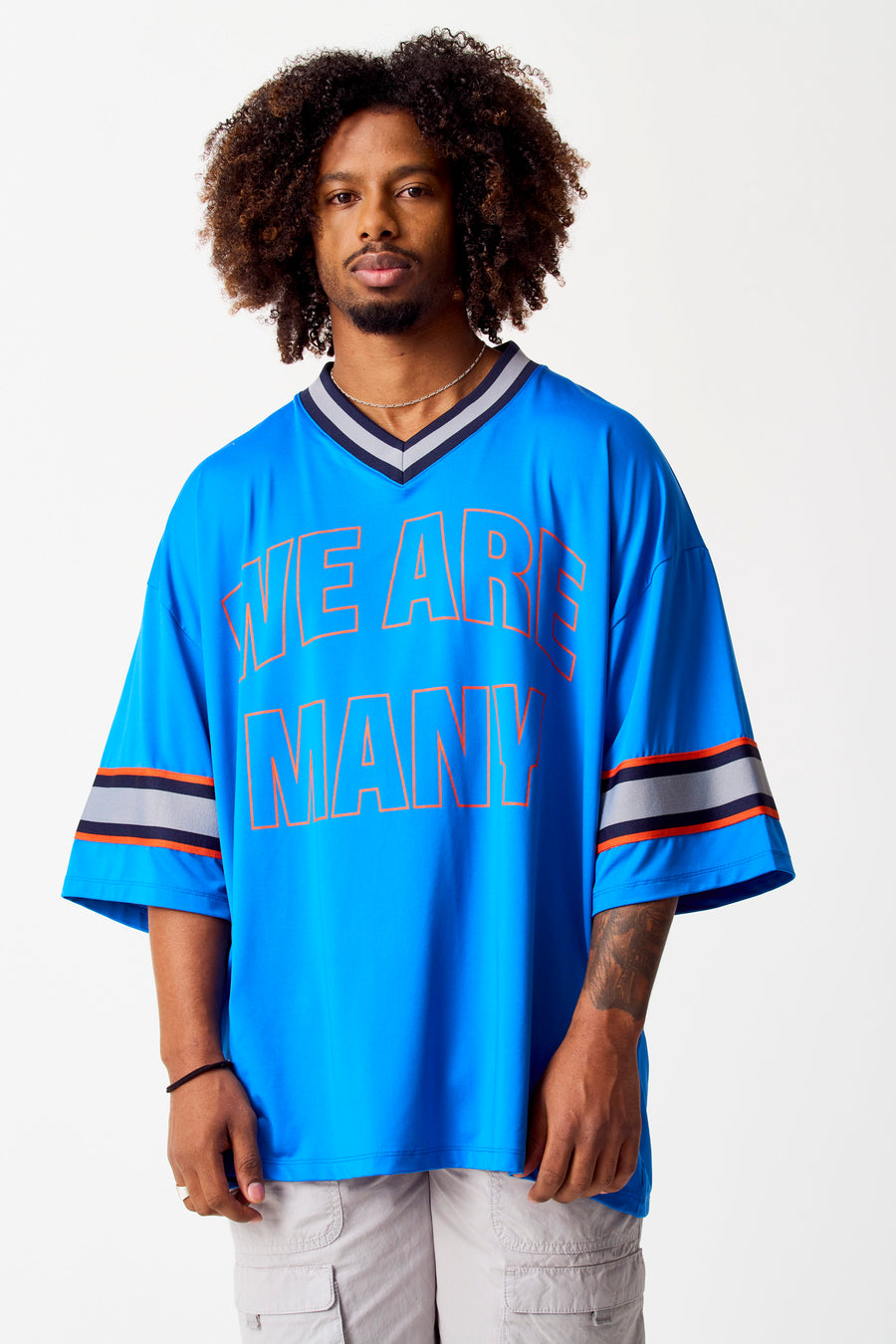 T-shirt bleu de COELY avec des manches courtes et le texte "WE ARE MANY" dessus, porté avec une chaîne et un cargo.