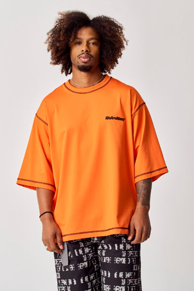T-shirt orange de COELY, avec des manches courtes et des boutons noirs, porté avec un pantalon imprimé.