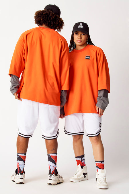 T-shirt orange de COELY, avec des manches grises longues en dessous, associé à des short de sport blancs et des chaussettes imprimées.