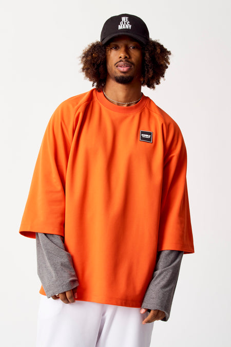 T-shirt orange à manches longues de COELY, avec un badge logo et un t-shirt gris en dessous.