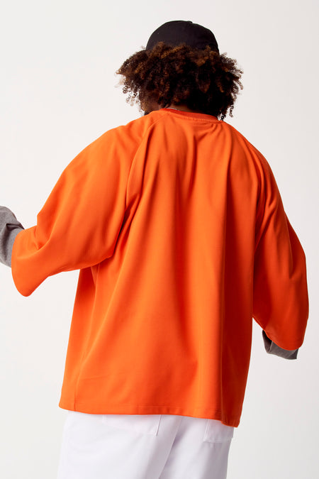 T-shirt orange à manches longues de COELY, vu de l'arrière, associé à un chapeau noir et des pantalons blancs.