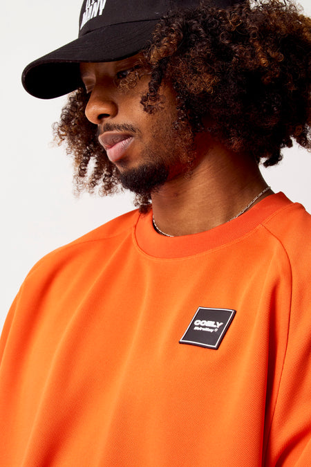 T-shirt orange à manches longues de COELY, avec un petit logo sur la poitrine et une chaîne.