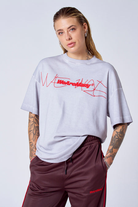 T-shirt gris à manches courtes de COELY, avec une impression de texte rouge et porté avec un pantalon de jogging bordeaux.