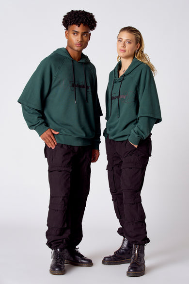 Sweat-shirt vert avec capuche de COELY, avec des cordons noirs et une inscription sur l'avant, porté avec un pantalon noir.