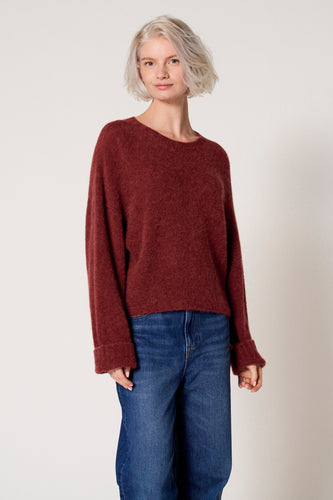 Een vrouw draagt een bordeauxrode trui en blauwe jeans.