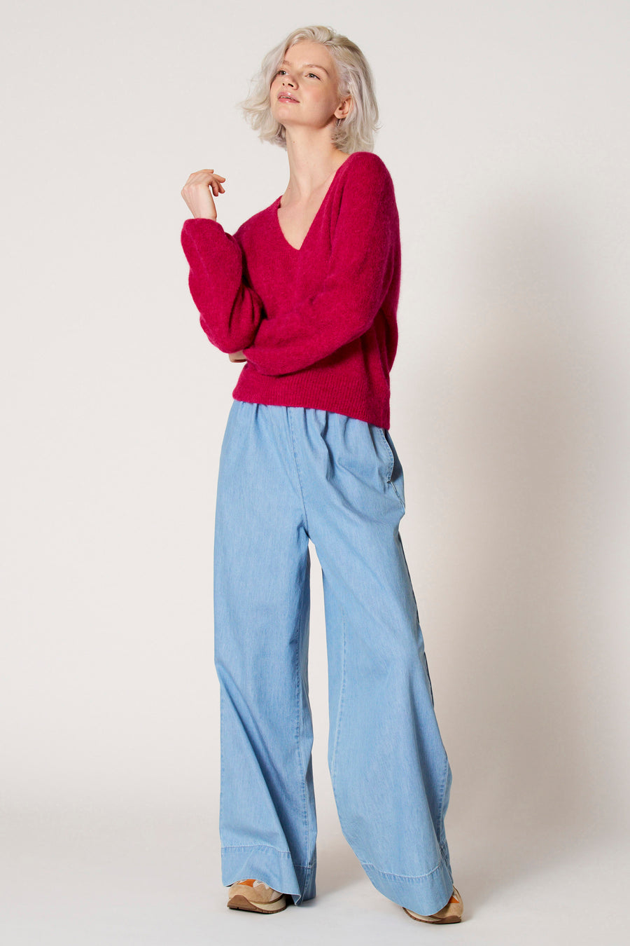 Pull à col V rose de Clouds of Fashion, associé à des pantalons bleus clairs larges et des chaussures brunes.