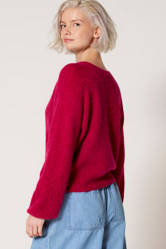 Pull à col V rose de Clouds of Fashion, porté avec un pantalon bleu clair.
