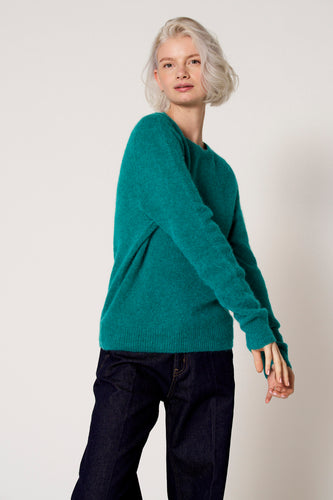 Vrouw met groene trui en donkere jeans.