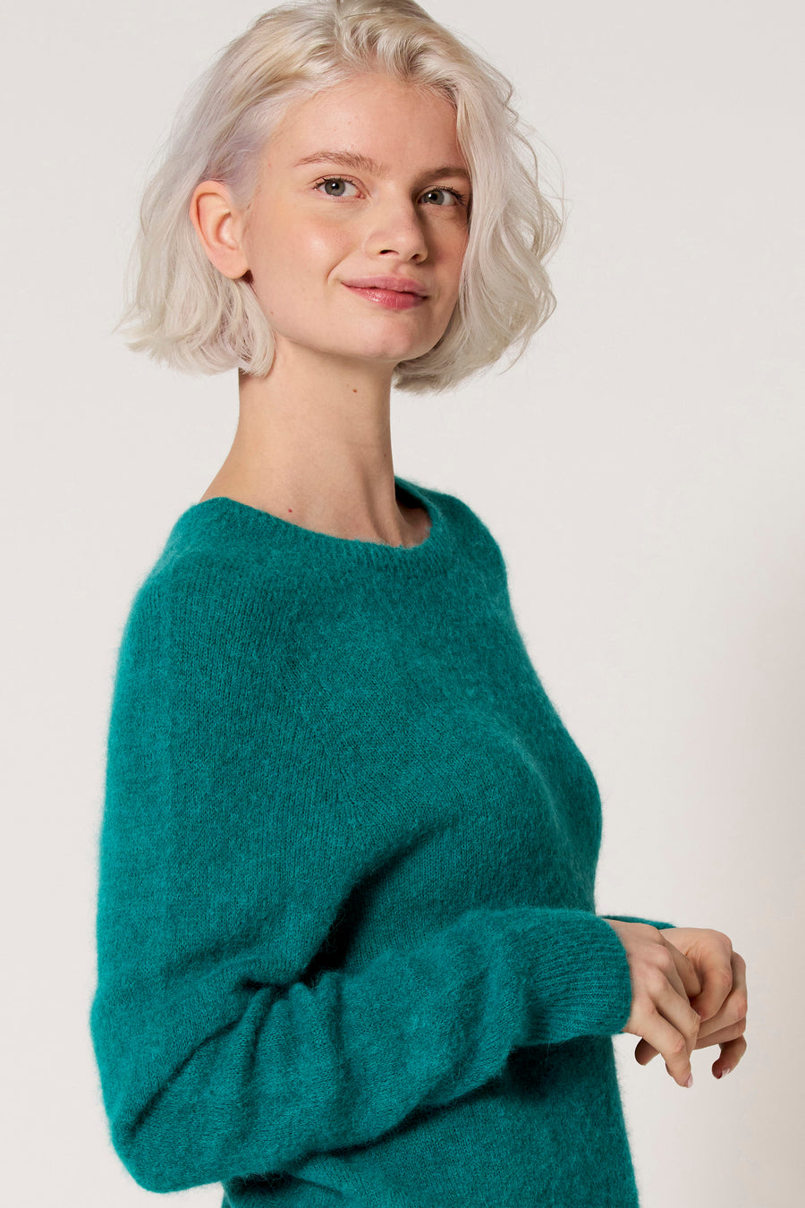 Vrouw met platinablond haar, groene mohair trui.