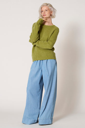 Vrouw met groene trui en wijde blauwe broek.
