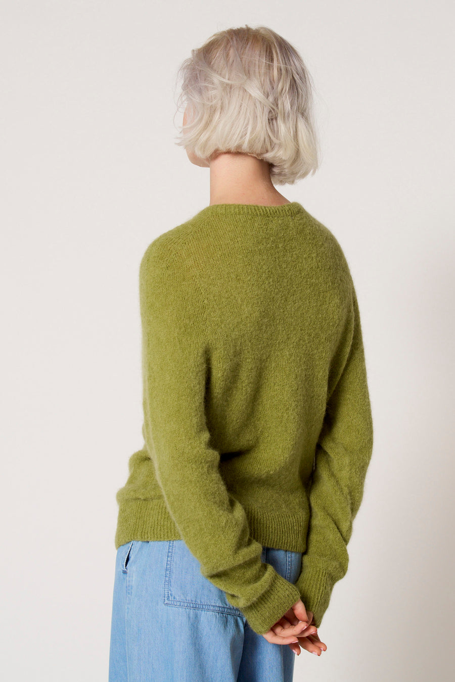 Achterkant van een vrouw met een groene trui en blauwe broek.