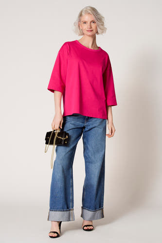 Sac à main noir de Clouds of Fashion, avec un mousqueton en or et porté avec un t-shirt rose et des jeans bleus.