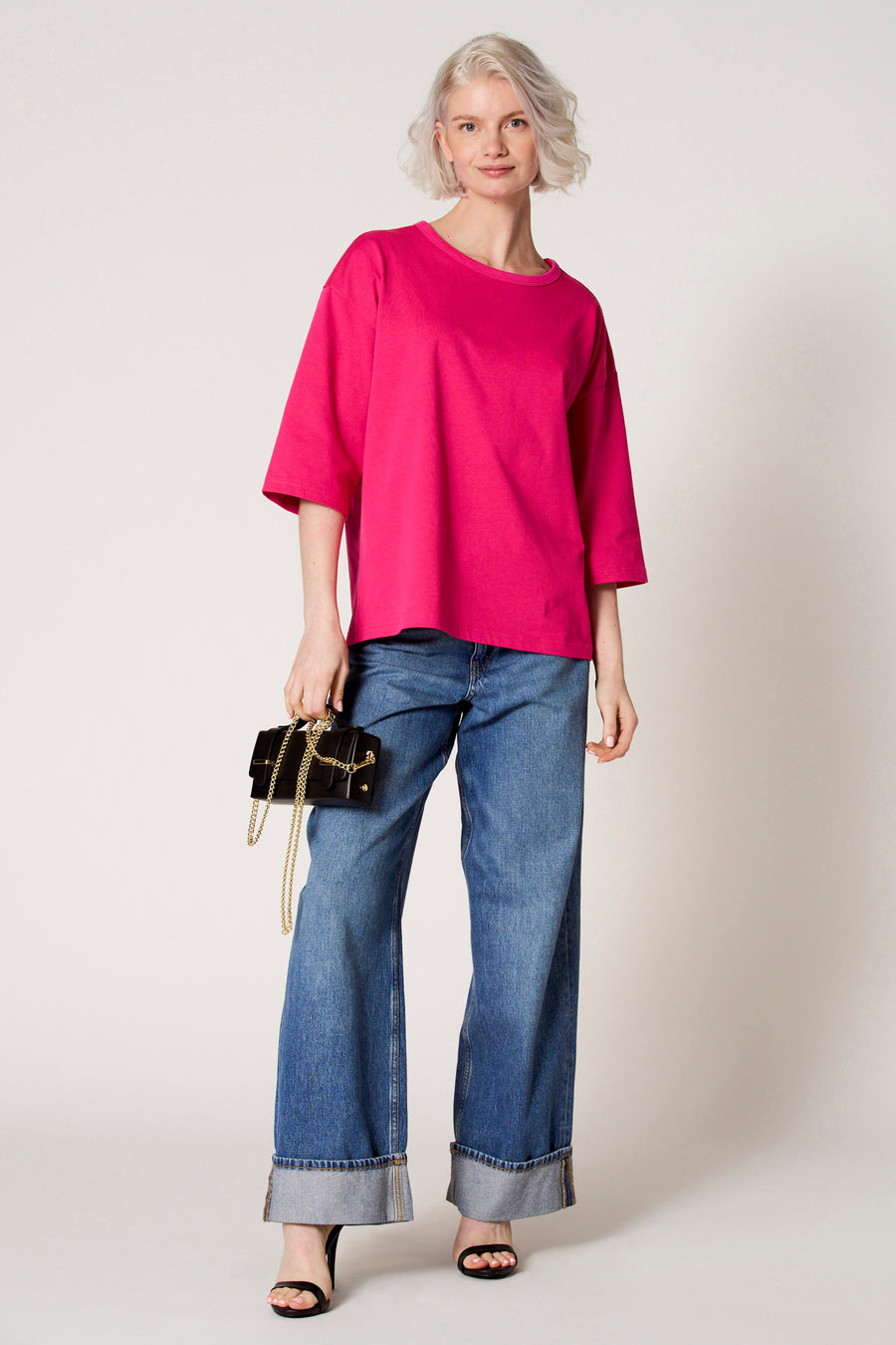 Vrouw in roze shirt, wijde jeans en zwarte sandalen met handtas.
