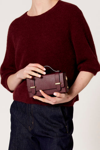 Vrouw met bordeauxrode trui en donkerblauwe jeans houdt bordeauxrode leren handtas vast.
