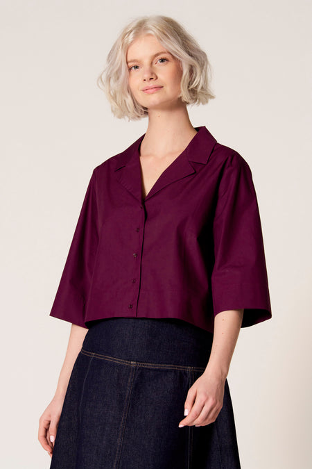 Chemisier violet à manches trois-quarts de Clouds of Fashion, avec fermeture à boutons et porté avec une jupe bleu foncé.