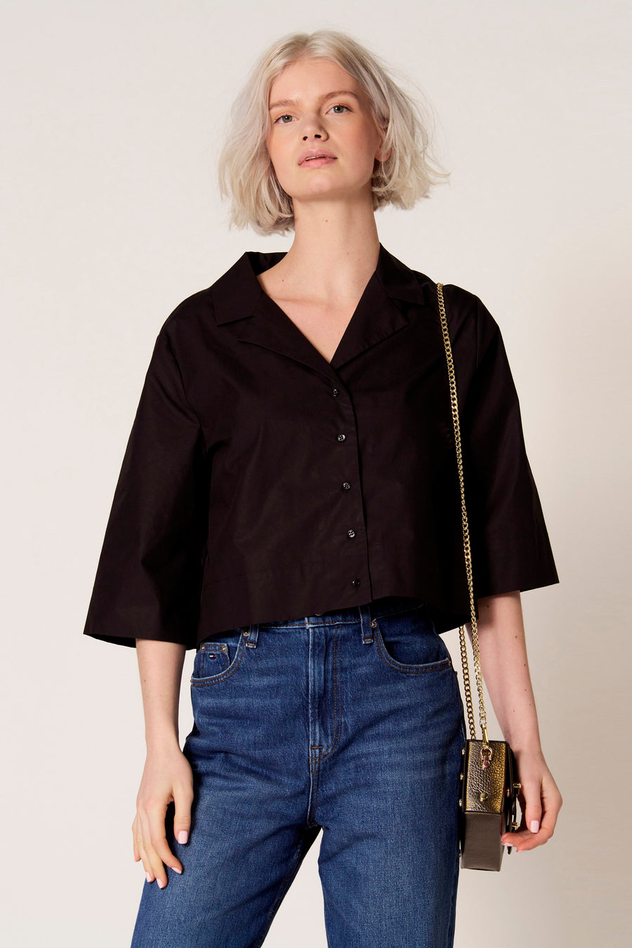 Chemisier noir de Clouds of Fashion, avec des manches courtes amples et un sac bandoulière doré.