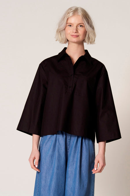 Chemisier noir à manches trois-quarts de Clouds of Fashion, avec fermeture boutonnée et poche poitrine, combiné avec un pantalon bleu.