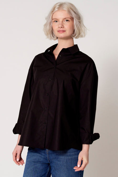 Chemisier noir à manches longues de Clouds of Fashion, avec fermeture boutonnée et manches retroussées, porté avec un jean.