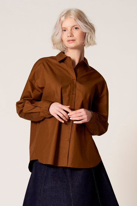 Chemisier marron à manches longues de Clouds of Fashion, avec fermeture à boutons et porté avec une jupe bleu foncé.