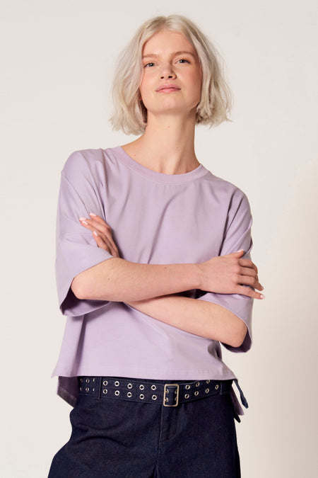 Paars T-shirt met korte mouwen van Clouds of Fashion, met losse pasvorm en gedragen met een donkerblauwe broek met riem.
