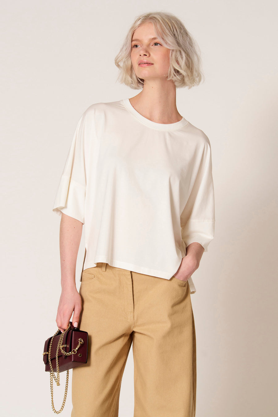 T-shirt écru à manches courtes de Clouds of Fashion, porté avec un pantalon kaki et un sac à main bordeaux avec chaîne dorée.