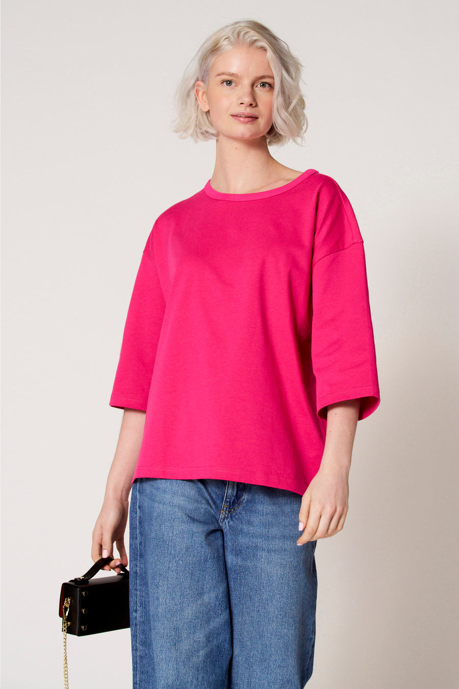 T-shirt rose à manches courtes de Clouds of Fashion, avec une coupe décontractée, associé à un jean bleu et un sac à main noir.