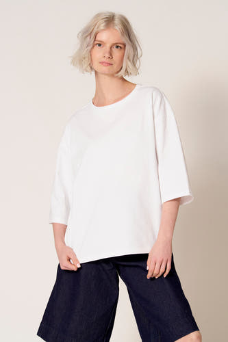 T-shirt blanc à manches courtes de Clouds of Fashion, combiné avec un pantalon évasé bleu foncé.