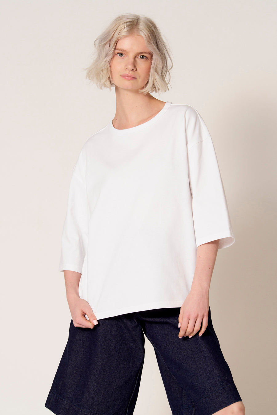 T-shirt blanc à manches courtes de Clouds of Fashion, combiné avec un pantalon évasé bleu foncé.