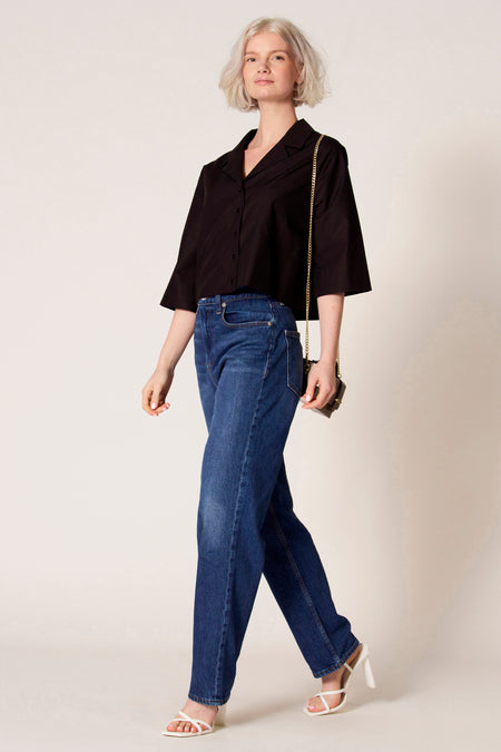 Blouse noire à manches trois-quarts de Clouds of Fashion, associée à des jeans bleu marine et des baskets blanches avec des lacets.