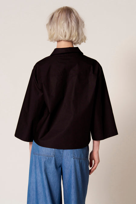 Blouse noire à manches trois-quarts de Clouds of Fashion, vue de derrière, avec un short en jeans bleu.