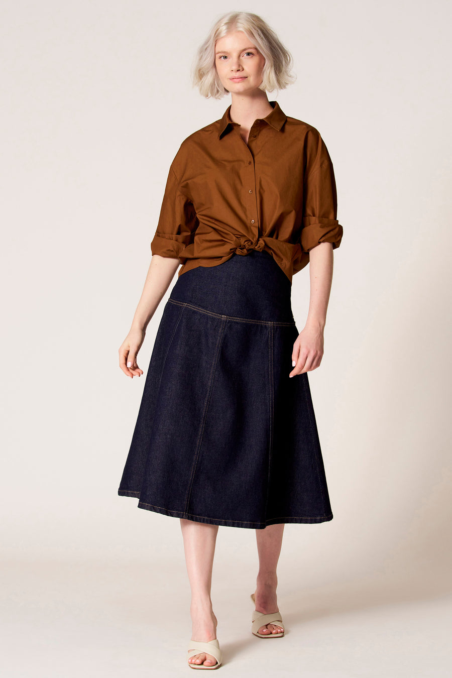 Blouse brune à longues manches de Clouds of Fashion, avec un col classique et des manches longues portées avec une jupe bleu marine.