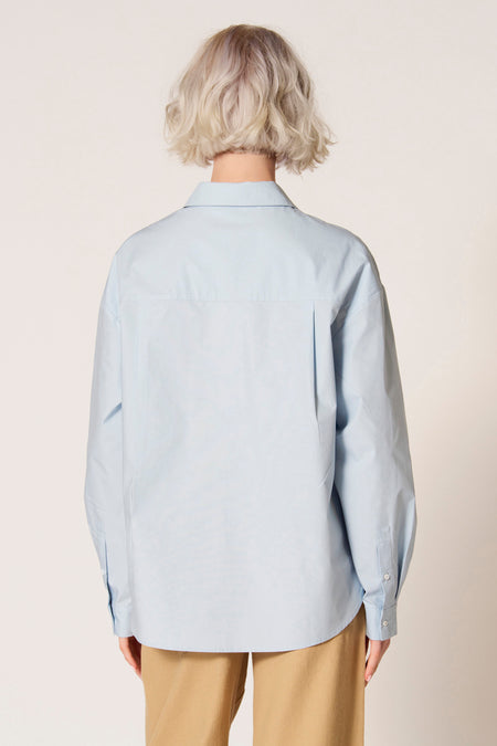 Blauw blouse met lange mouwen van Clouds of Fashion, gezien van achteren, met een subtiele plooi en lichtgekleurde broek.
