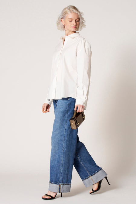 Blouse blanche à longues manches de Clouds of Fashion, portée avec des jeans larges et des talons noirs, en vue latérale.