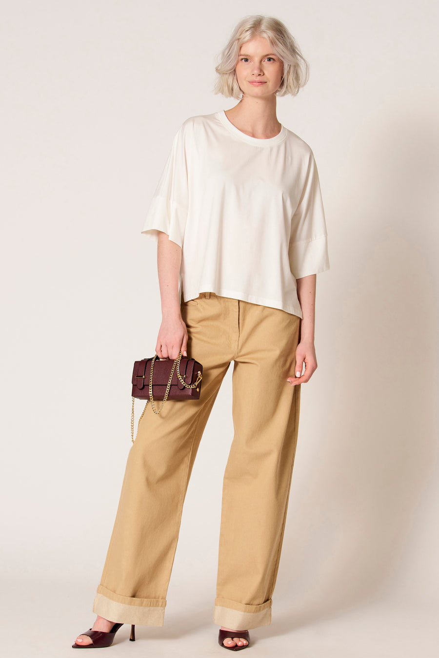 T-shirt écru à manches courtes de Clouds of Fashion, avec des manches amples et une subtile fente sur le côté, combiné avec un pantalon marron.