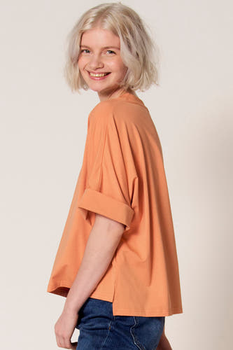 T-shirt à manches courtes orange de Clouds of Fashion, avec manches retroussées et coupe décontractée, combiné avec un jean foncé.