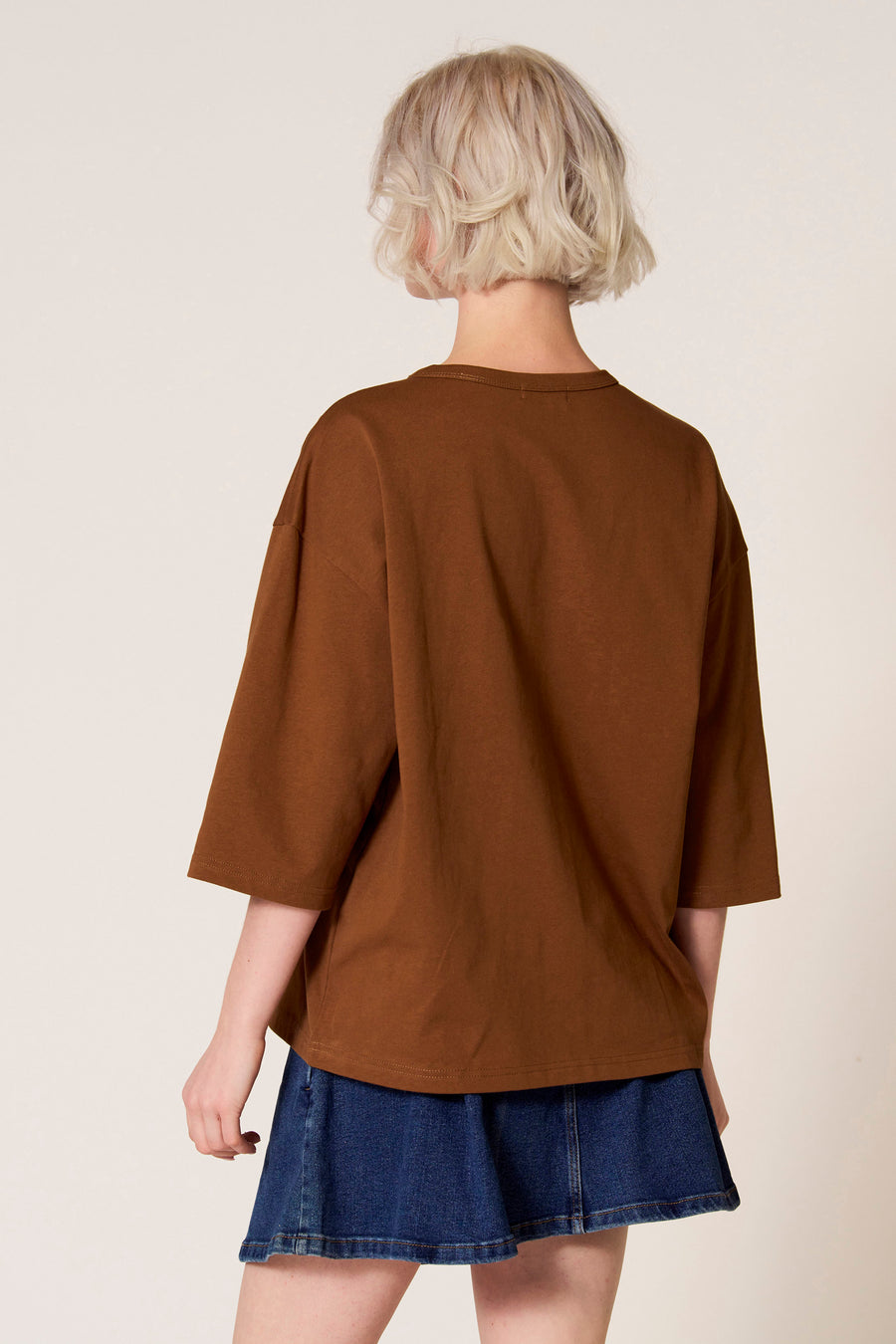 Bruin T-shirt met korte mouwen van Clouds of Fashion, gezien van achteren, gecombineerd met een denim rok.
