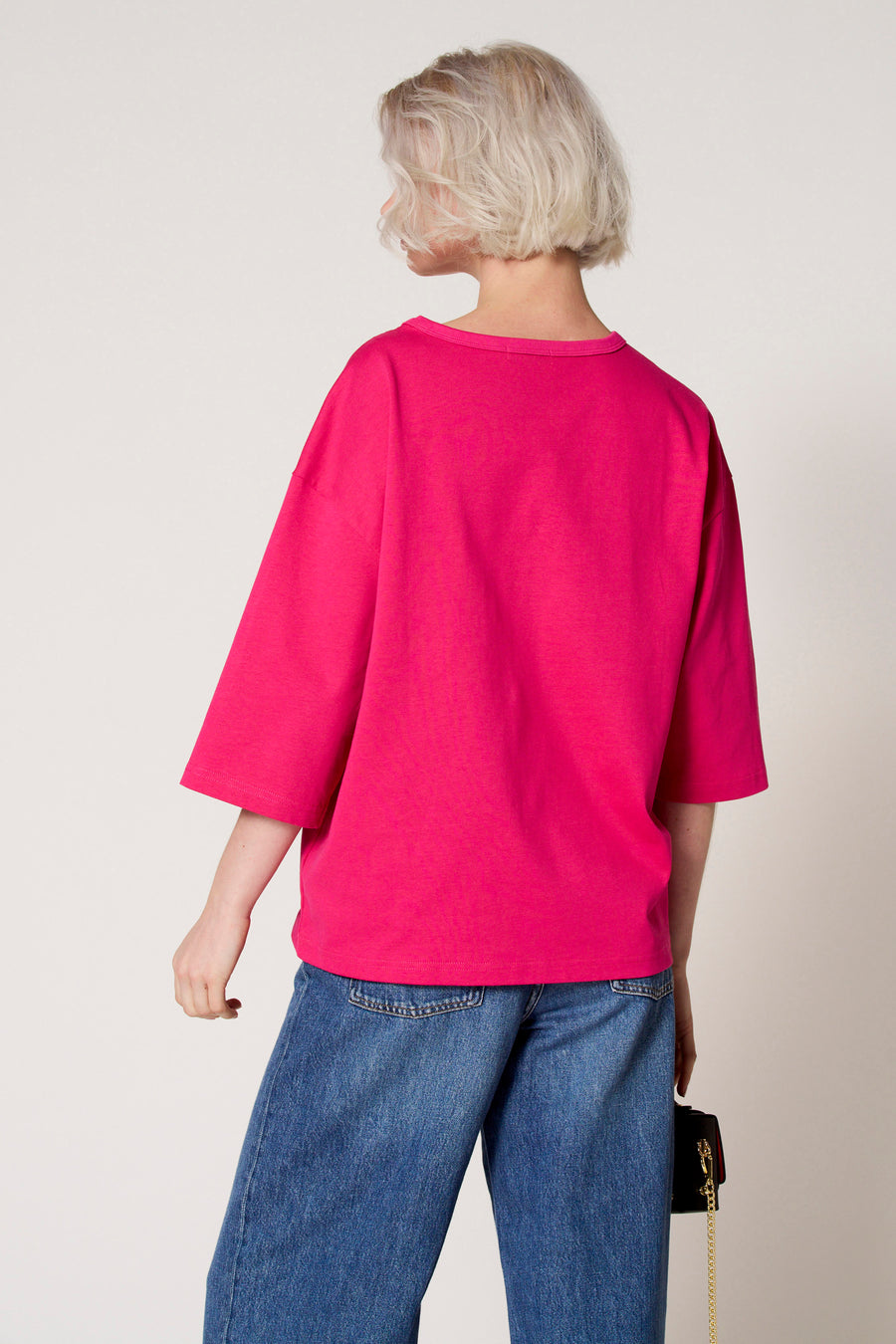 T-shirt à manches courtes rose de Clouds of Fashion, vu de dos avec un jean bleu et un sac à main noir avec chaîne dorée.