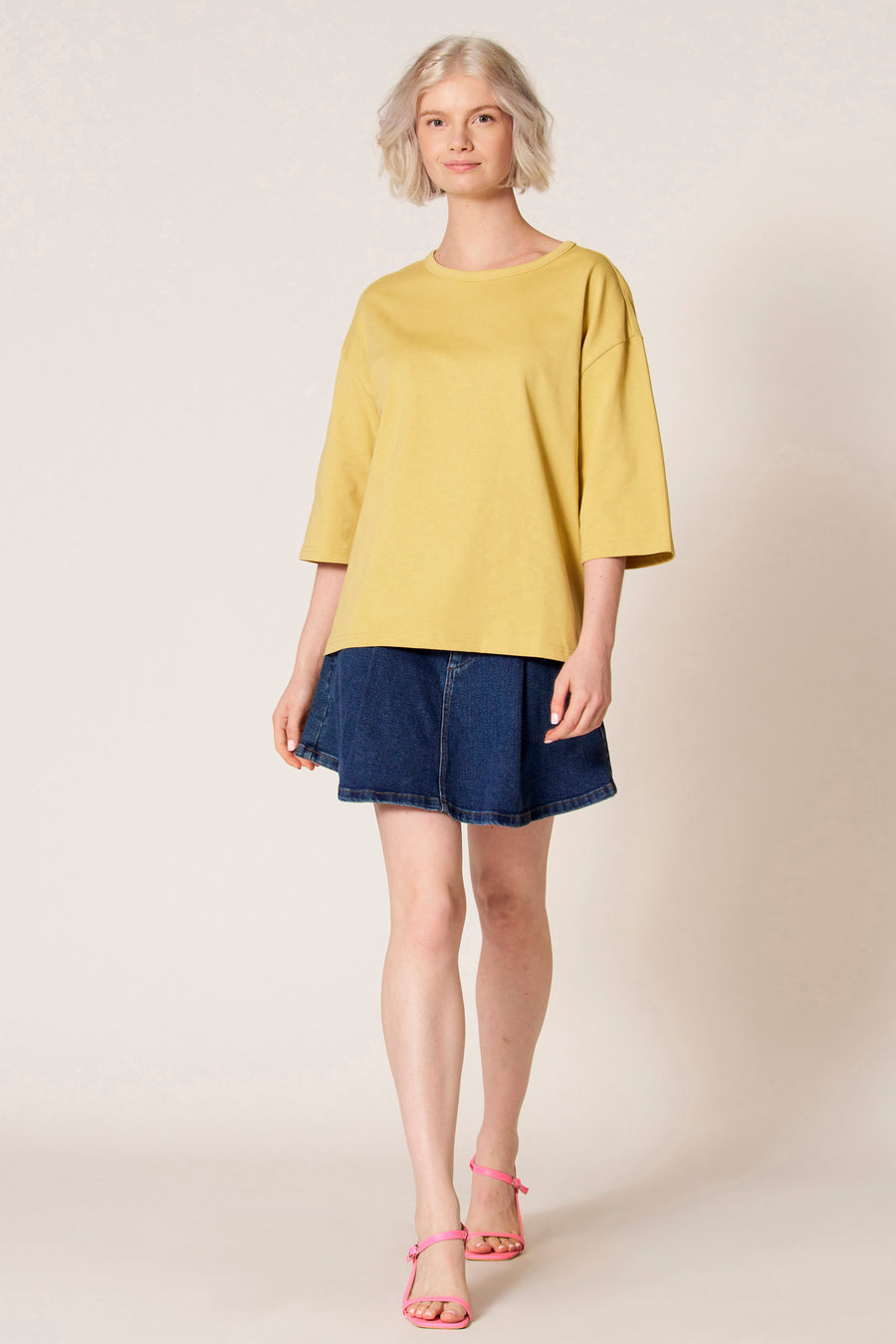 T-shirt à manches courtes jaune de Clouds of Fashion, avec une coupe ample et associé à une jupe en jean bleue.