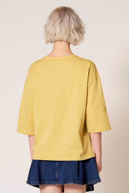 Geel T-shirt met korte mouwen van Clouds of Fashion, met een losse pasvorm en gecombineerd met een blauwe denim rok.
