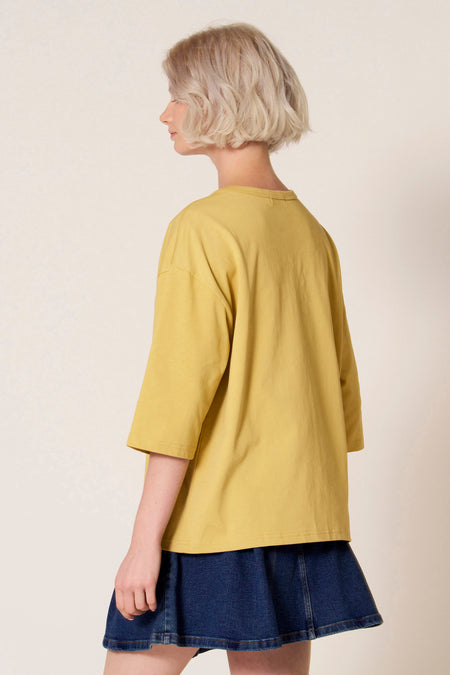 Geel T-shirt met korte mouwen van Clouds of Fashion, gedragen met een denim minirok, rugaanzicht.
