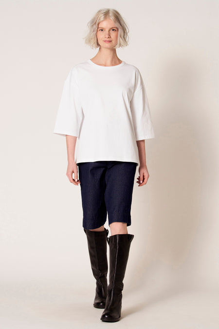 Wit T-shirt met korte mouwen van Clouds of Fashion, gedragen met donkerblauwe denim shorts en zwarte leren laarzen.